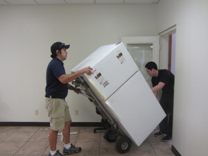 two long-distance movers bringing in a refrigerator using a dolly